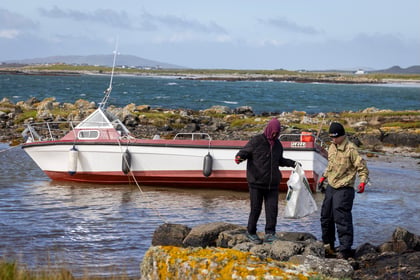 Two young adults doing beach clean up with boat and sea in background