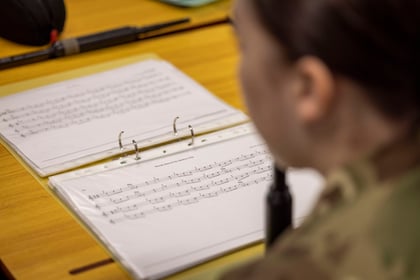 female cadet looking at the music on her page to play a bagpipe.