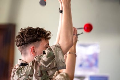 male cadet with brown curly hair in military uniform with hands in the air holding drum sticks