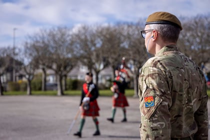 male instructor with grey hair in in military uniform stood watching cadets performing on their bagpipes