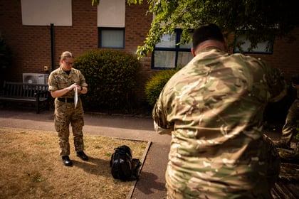 2 adults in military uniform stood outside a building on the grass practicing first aid with a bandage