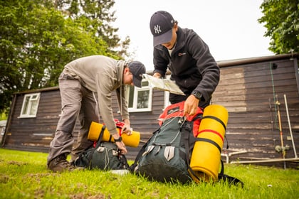 2 cadets packing kit outside of building on the grass into green bags with yellow roll mats attached