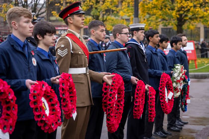 Line of cadet from various military services holding red poppy wreaths, one army cadet in brown uniform with peak hat.