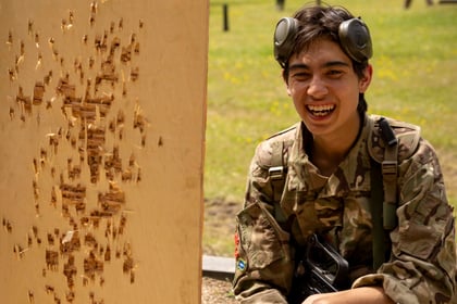 Cadet in military uniform with short hair looking at his sots on the target and smiling