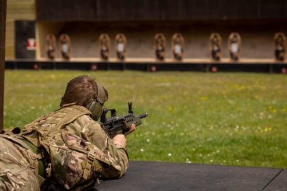cadet shooting on a grass range in military uniform with the targets in the distance