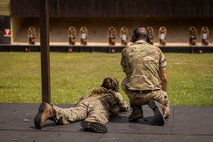 cadet laying on the floor at a short grass shooting range being spoken to by an adult kneeling down next to him