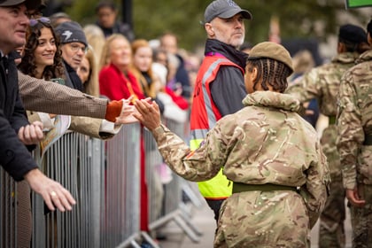black cadet with braids in military uniform with olive green beret facing away and high fiving spectators behind a barrier