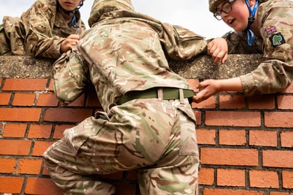 cadet climbing over a wall being helped by 2 friends