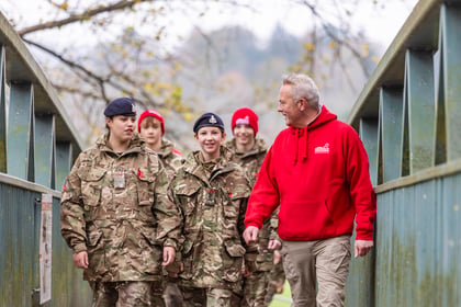 Cadets in military uniform walking over a bridge with a man in a bright red jumper
