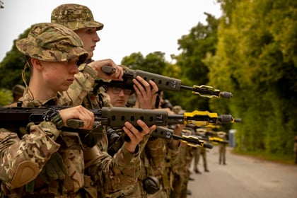 cadets in a line with weapons rested on their shoulders in military uniform with military bucket hats on.