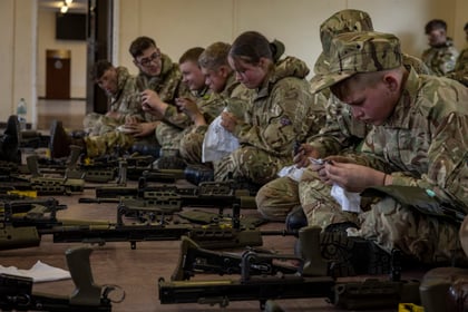 line of cadets sat on the floor cleaning weapons with white cloths