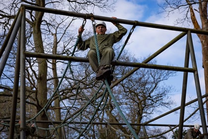 cadet in olive green overalls coming down a rope from a metal structure