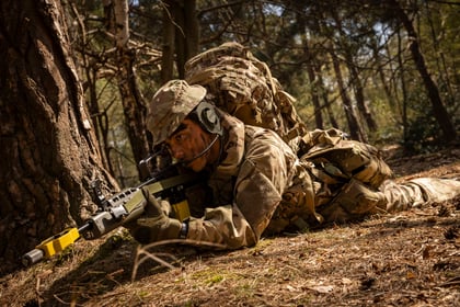 cadet laying down in the woods wearing camo clothing and holding a weapon