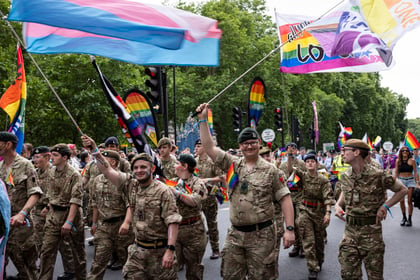 Smiling cadets and volunteers walking in the Pride in London Parade while waving flags
