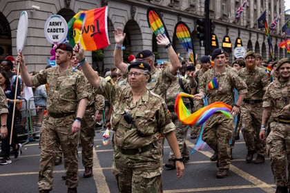 Adult volunteers and cadets wave at spectators at Pride in London waving pride flags