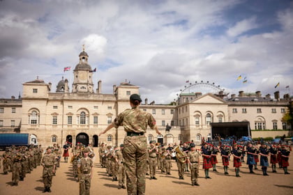 Band master stands with her back to the camera with London buildings in the background as well as London Eye