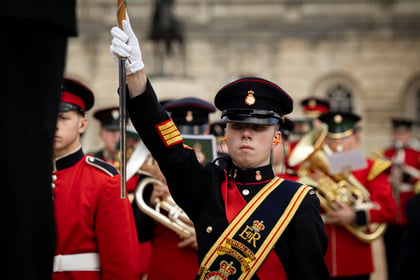 Ceremonial cadets in a colourful military band saluting and playing instruments during a parade in central London.