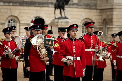 Cadets dressed in ceremonial attire play brass instruments while marching at Horse Guards in London.