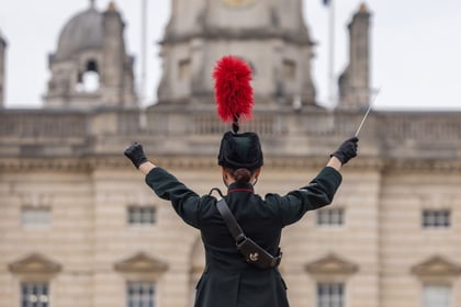 Band master with her back turned to the camera with Horse Guards in the background