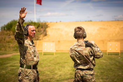 Adult volunteer stands with hand up on shooting range