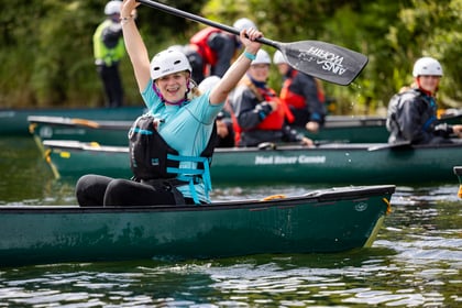 Adult volunteer in canoe hold paddle above head and smiles for the camera