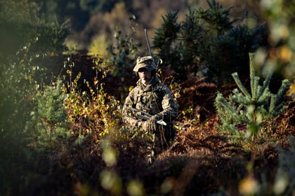 cadet in camouflage uniform hiding in a bush with a green camouflage bucket hat