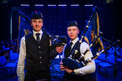 Cadets holding bagpipes pose for a photo with a stage in the background
