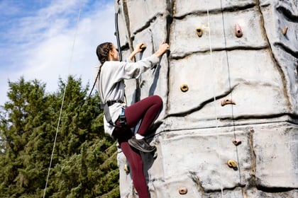 Female cadet climbs the climbing wall with supportive wires