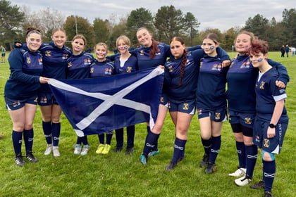 Female cadets from Scotland wearing rugby uniform holding Scottish flag