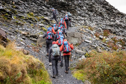 Group of cadets and volunteers walk up a mountain with rocks along the path