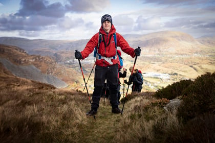 Male cadet stands with walking sticks in his hands on top of the mountain