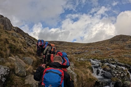 Group of cadets climb up a mountain with red and blue backpacks on