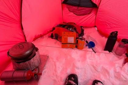 Person sits in tent with supplies in snow