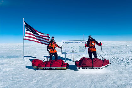 Jordan Wylie poses with American flag and expedition partner at Geographic South Pole