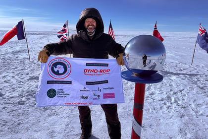 Jordan Wylie poses with sponsor flag at South Pole marker