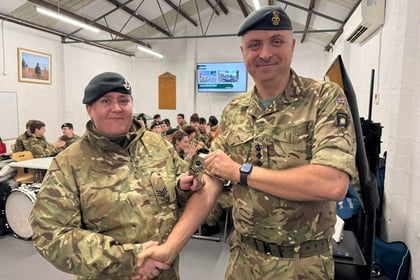 2 people in military uniform smiling at camera in a hall, shaking hands