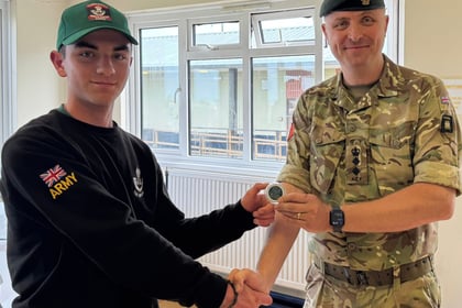 Man in military uniform stood shaking person in black jumper and green baseball caps hand