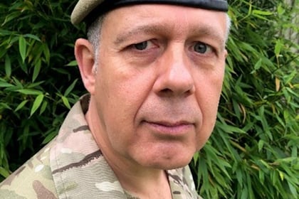 Head shot of a man with gray hair in military uniform wearing an online green beret looking at the camera