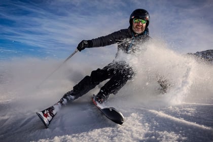 Adult volunteer sprays snow at the camera with a smile on his face