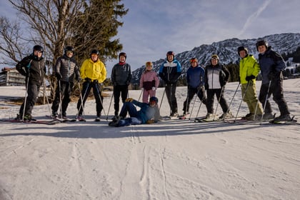 Group of adult volunteers pose on ski slope while learning to ski in Bavaria