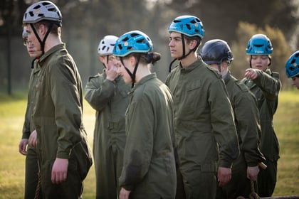 Cadets with blue and grey helmets stand in dark green overalls