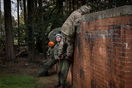 Cadets help the Brigadier over a brick wall on the obstacle course