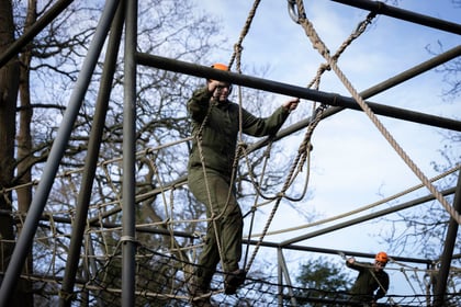 A cadet dressed in overalls and orange helmet on obstacle course