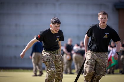 Two male cadets pull something across a sports field