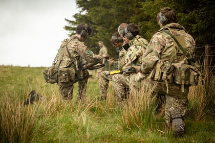 Cadets kneel by a wired fence reloading their weapons