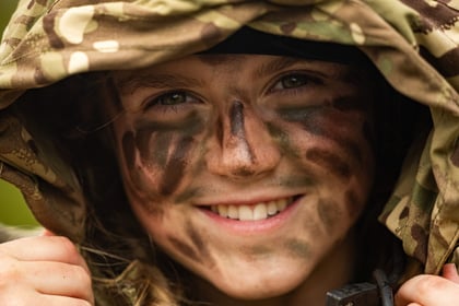 Female cadet smiles at the camera wearing camo cream and a hood over her head