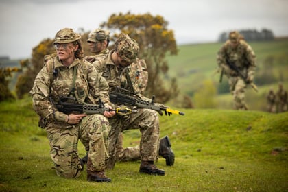 Female cadet looks out at field while holding a weapon and kneeling
