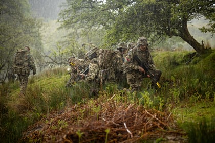 Cadets kneel in the brush while it pours with rain