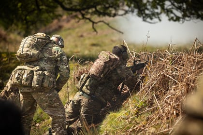 Cadet looks over the verge of a grassy patch with adult instructor looking on