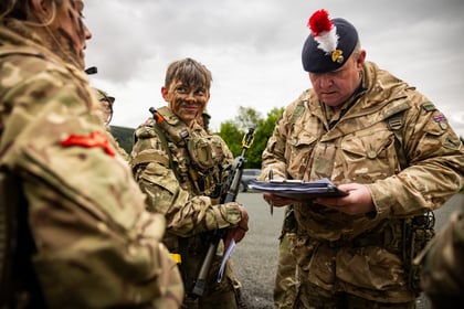 Adult instructor looks down at a sheet of paper while male cadet smiles